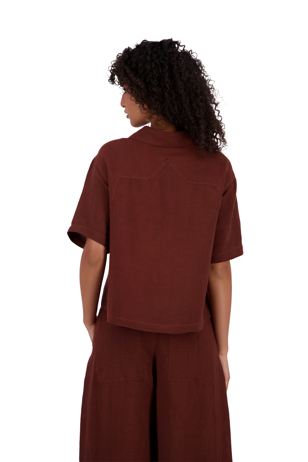 A model shown from the back wearing a rust-brown short-sleeve collared shirt and matching wide-leg pants against a solid white background. #Burnt_Clove