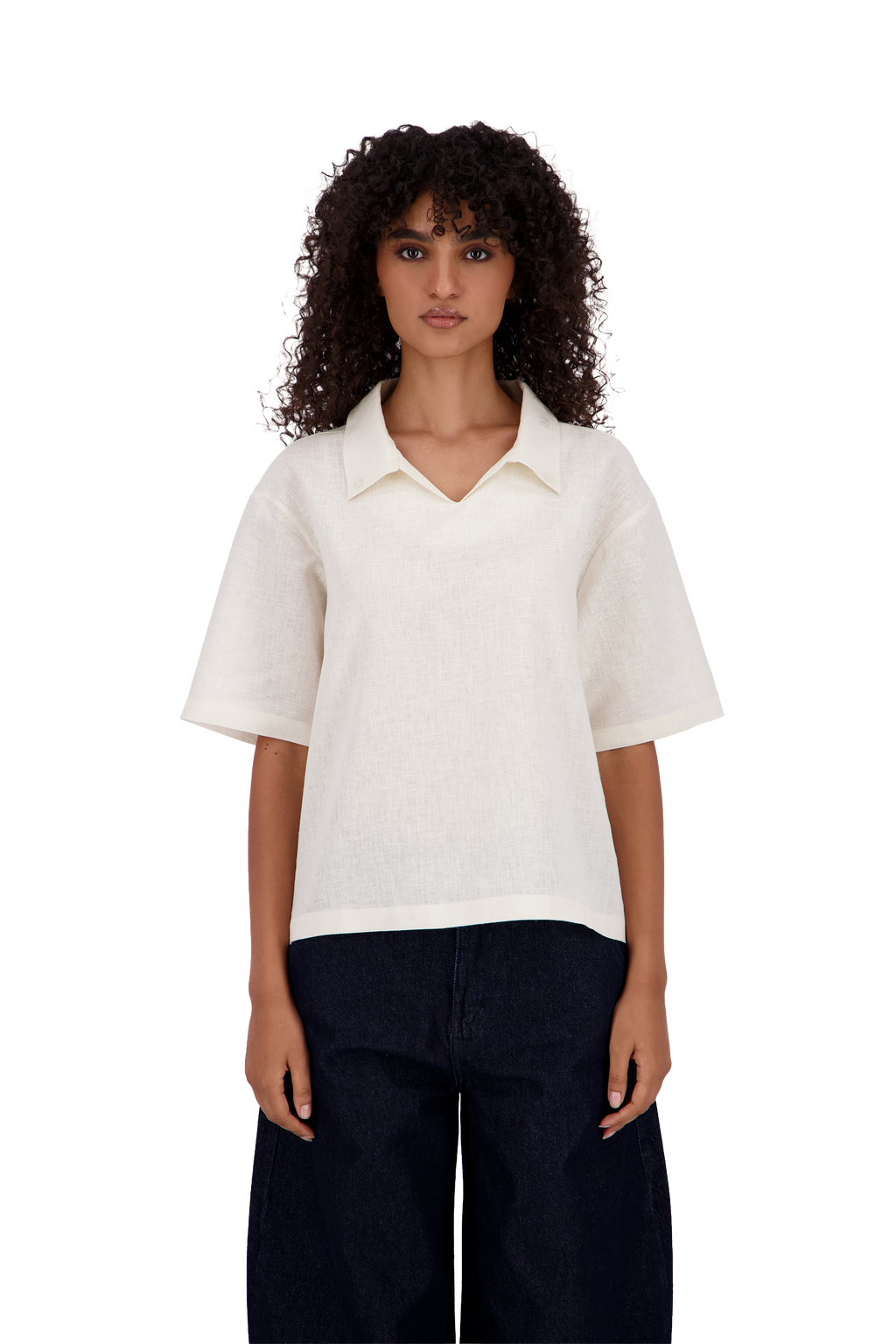 A model with curly dark hair wearing a short-sleeve, collared knit top in off-white and dark navy pants, shot against a solid white background. #Milk_Dune