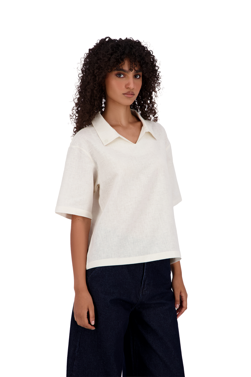 A model with curly dark hair wearing a short-sleeve white knit polo shirt and dark wide-leg jeans, photographed against a solid white background. #Milk_Dune