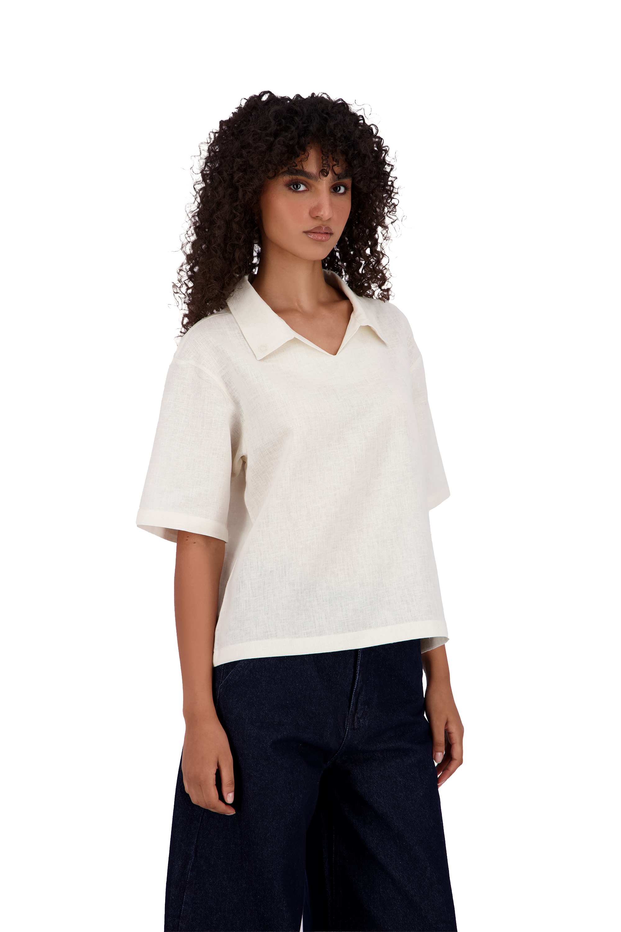 A model with curly dark hair wearing a short-sleeve white knit polo shirt and dark wide-leg jeans, photographed against a solid white background. #Milk_Dune